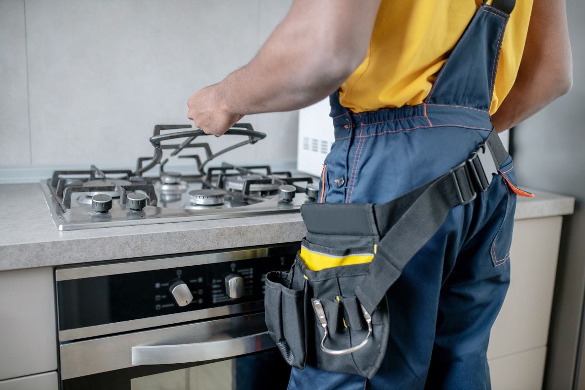 Certified technician servicing gas stove burner in professional kitchen setup
